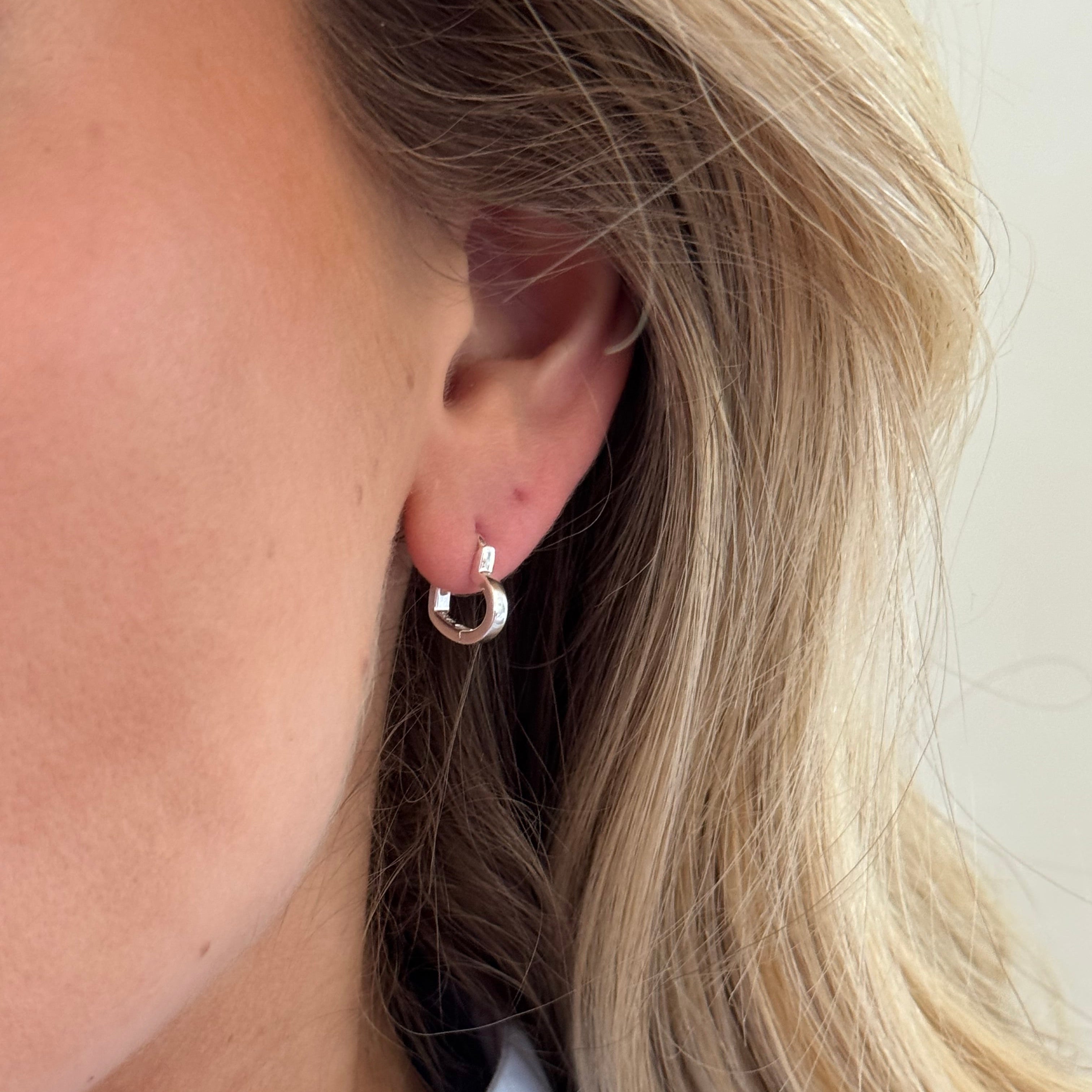 Close-up of an ear with a gold hoop earring against a neutral background