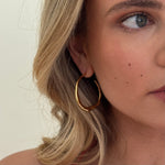Close-up of a woman wearing a gold hoop earring with a neutral background