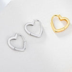 Heart-shaped earrings in silver and gold on a light gray background