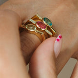 Gold ring with multicolored gemstones on a person's finger against a neutral background