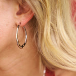 Close-up of a person wearing a silver hoop earring with blonde hair.