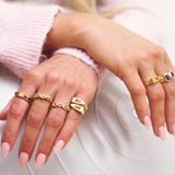 Close-up of hands wearing gold rings on a light background