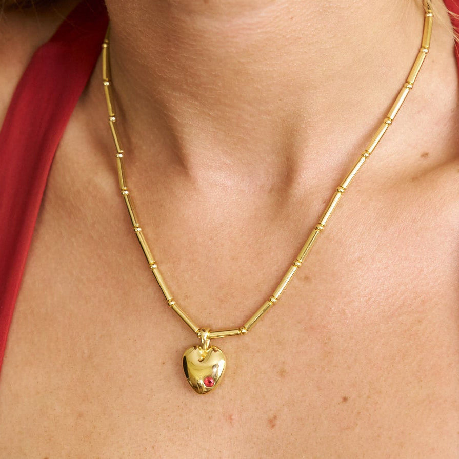 Gold necklace with a heart pendant worn by a person in a red garment.