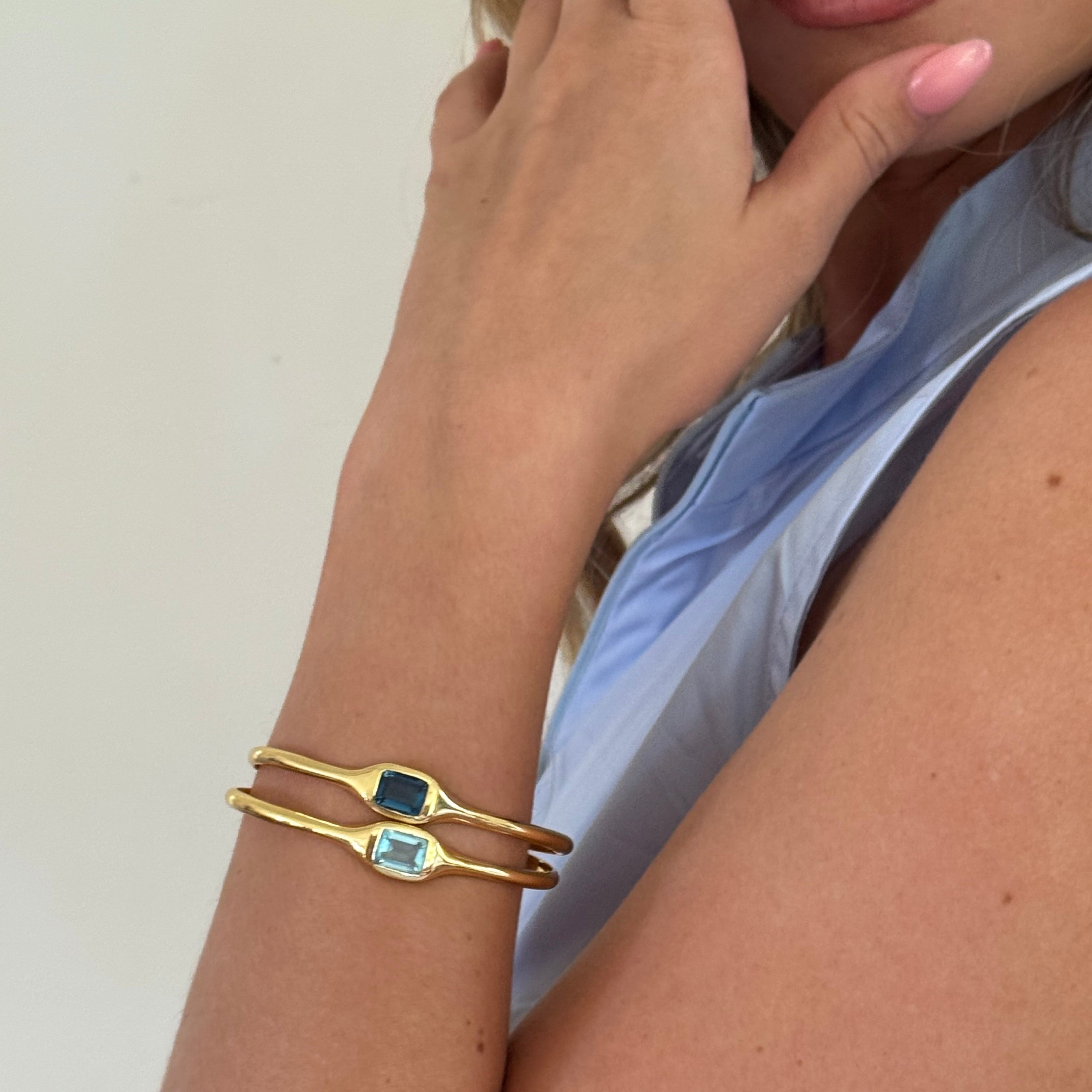 Gold bracelet with gemstones on a person's wrist against a neutral background