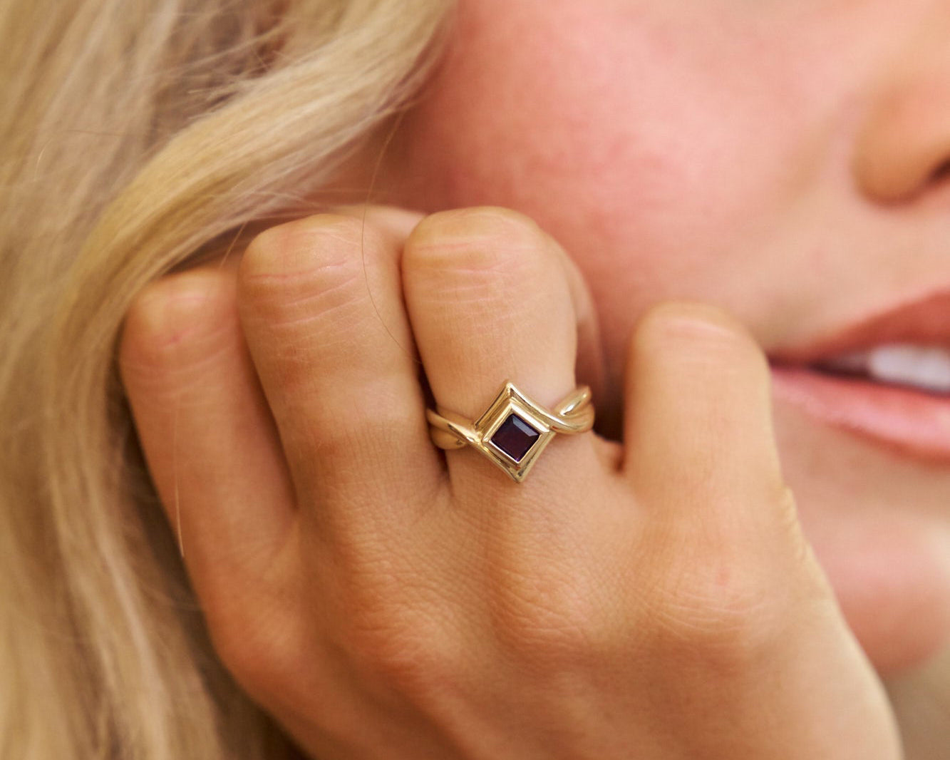 Close-up of a hand wearing a gold ring with a blue gemstone, held near the face.