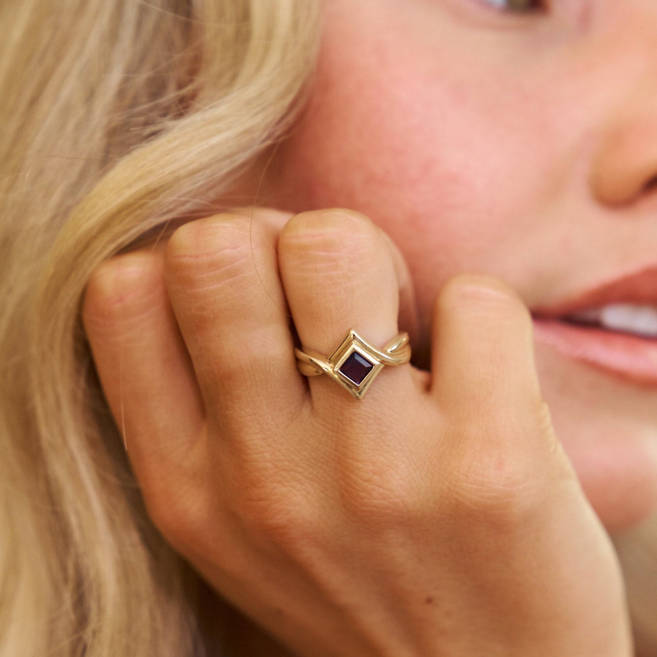 Close-up of a hand wearing a gold ring with a blue gemstone, held near the face.