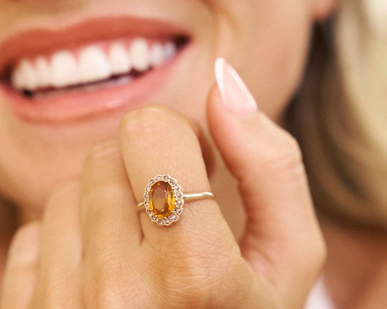 Close-up of a woman's hand wearing a ring with a yellow gemstone, blurred background