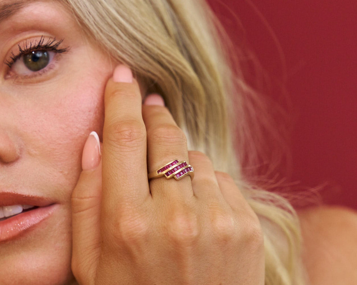 Close-up of a woman's face with a hand touching her cheek, wearing a pink ring.