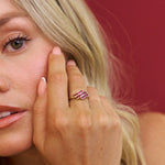 Close-up of a woman's face with a hand touching her cheek, wearing a pink ring.