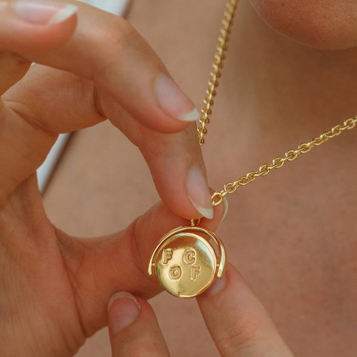Gold necklace with a round pendant held by a hand