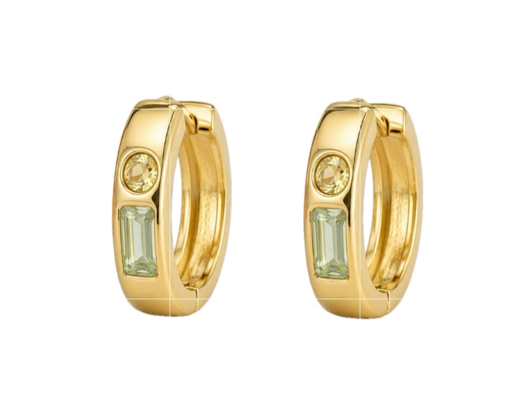 A pair of gold huggie hoop earrings, each featuring a small round clear stone and a larger rectangular light green baguette-cut stone, shown on a plain white background.