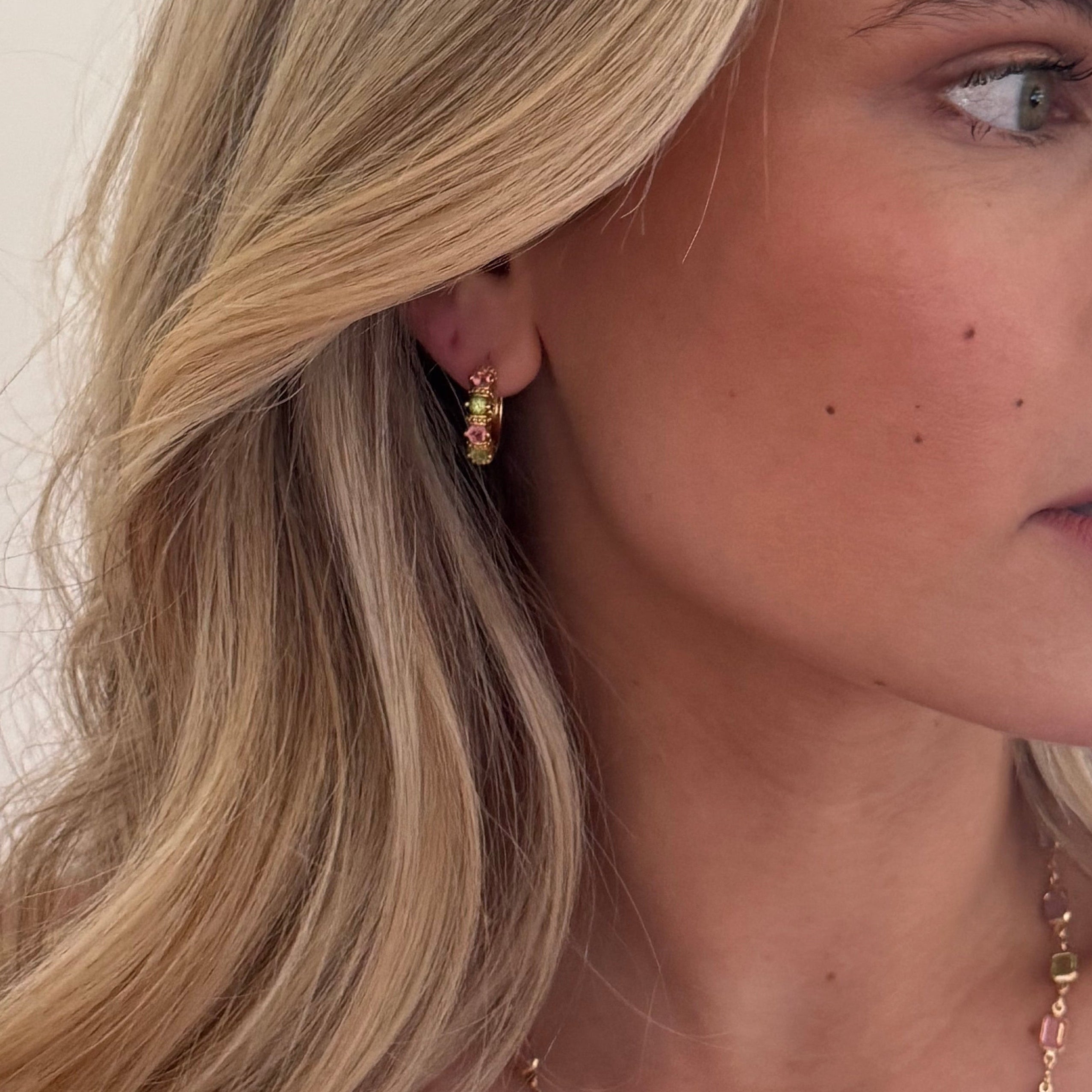 Woman with blonde hair and a red top against a white background modelling jewellery