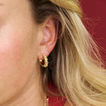 Close-up of a person wearing gold hoop earrings with a red background