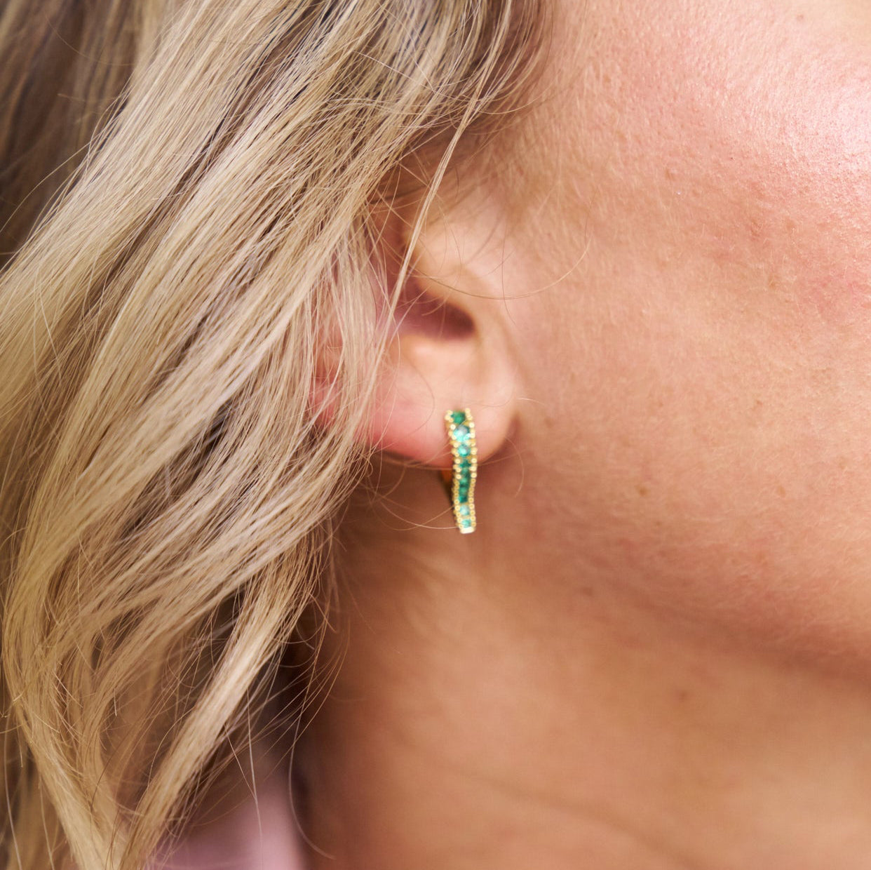 Close-up of an ear wearing a green hoop earring with blonde hair.