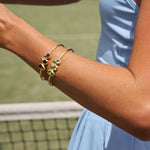 Close-up of a person wearing gold bracelets on a blurred outdoor background