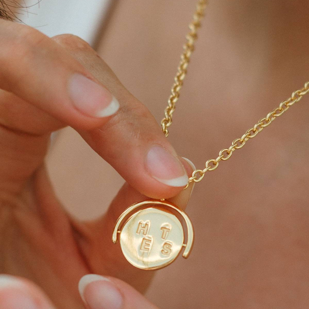 Gold necklace with a round pendant held by a hand against a blurred background