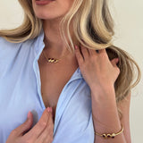 Woman lying down with hands on her hair and chest, wearing a gold bracelet and necklace.