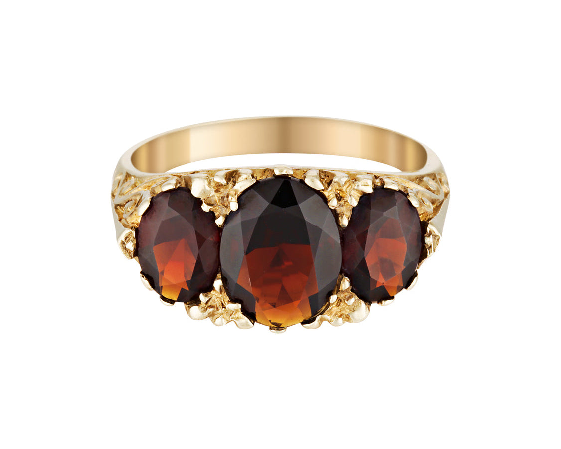 Gold ring with three dark red garnet gemstones on a white background
