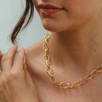 Close-up of a person wearing a gold chain necklace and bracelet against a neutral background
