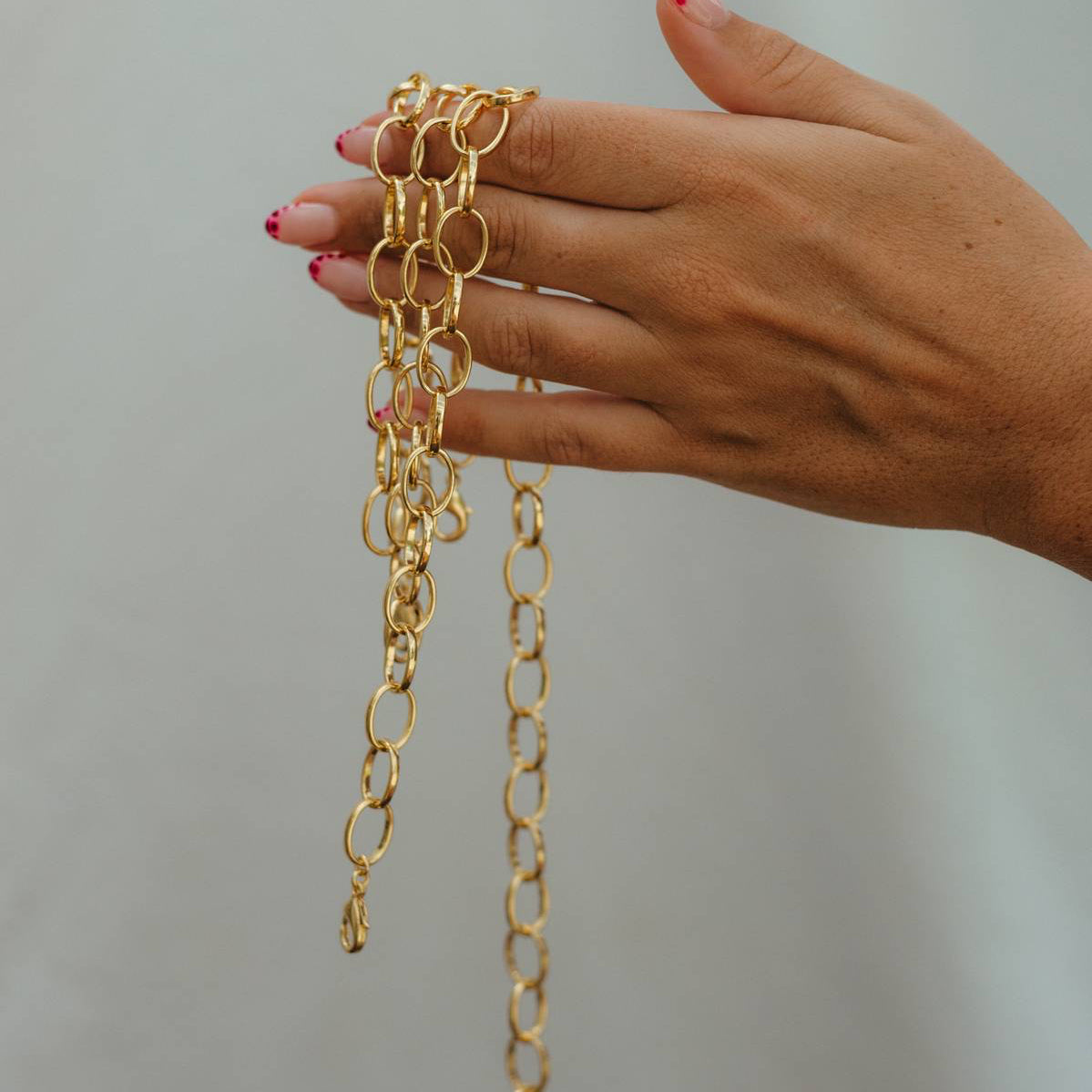 Hand holding gold chain necklaces against a plain background