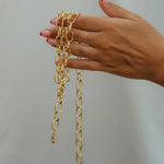 Hand holding gold chain necklaces against a plain background