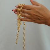 Hand holding gold chain necklaces against a plain background
