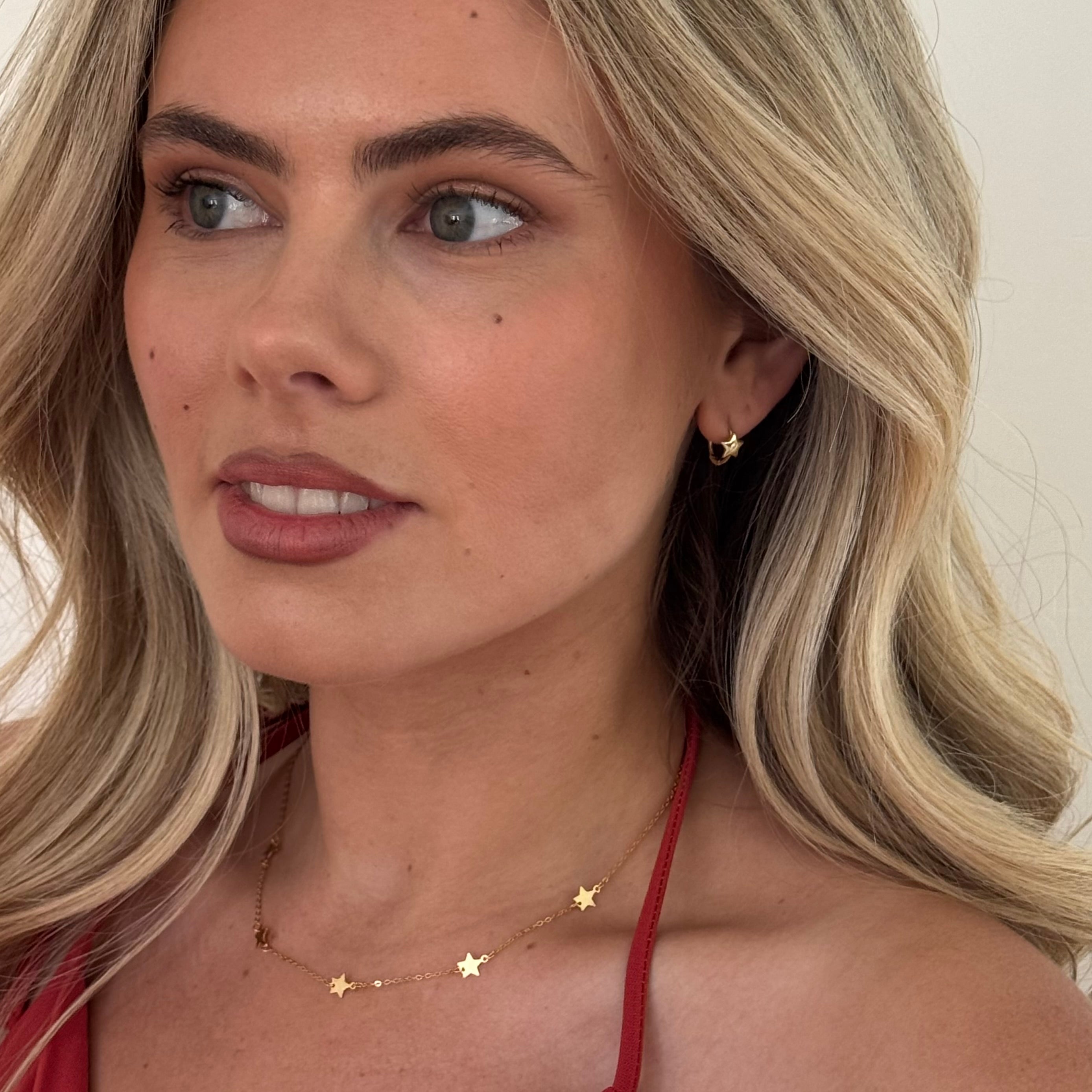 Close-up of a woman with blonde hair wearing gold earrings and a star-shaped necklace.