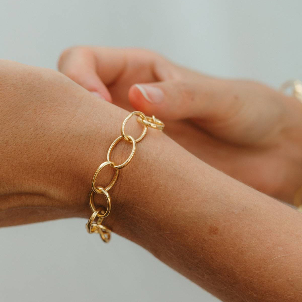Gold chain bracelet on a wrist against a neutral background