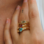 Close-up of a hand wearing three gold rings with colored gemstones.