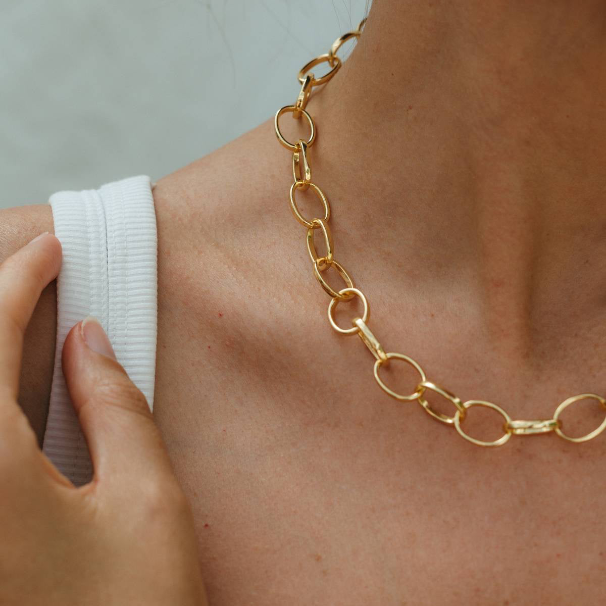 Gold chain necklace being worn on a person's neck with a blurred background