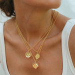 Close-up of a person wearing a gold necklace with coin pendants on a white background