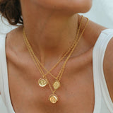 Close-up of a person wearing a gold necklace with coin pendants on a white background