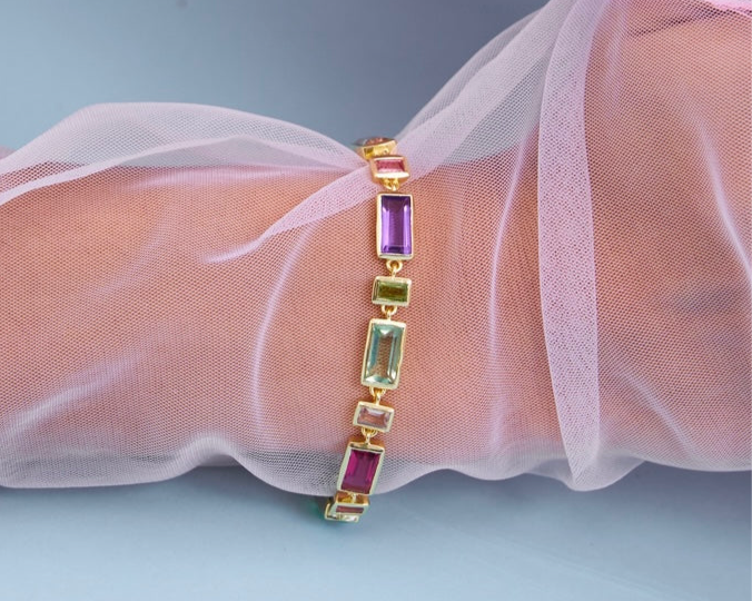 Multicolored gemstone bracelet on a wrist with sheer fabric background