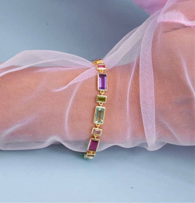Multicolored gemstone bracelet on a wrist with sheer fabric background