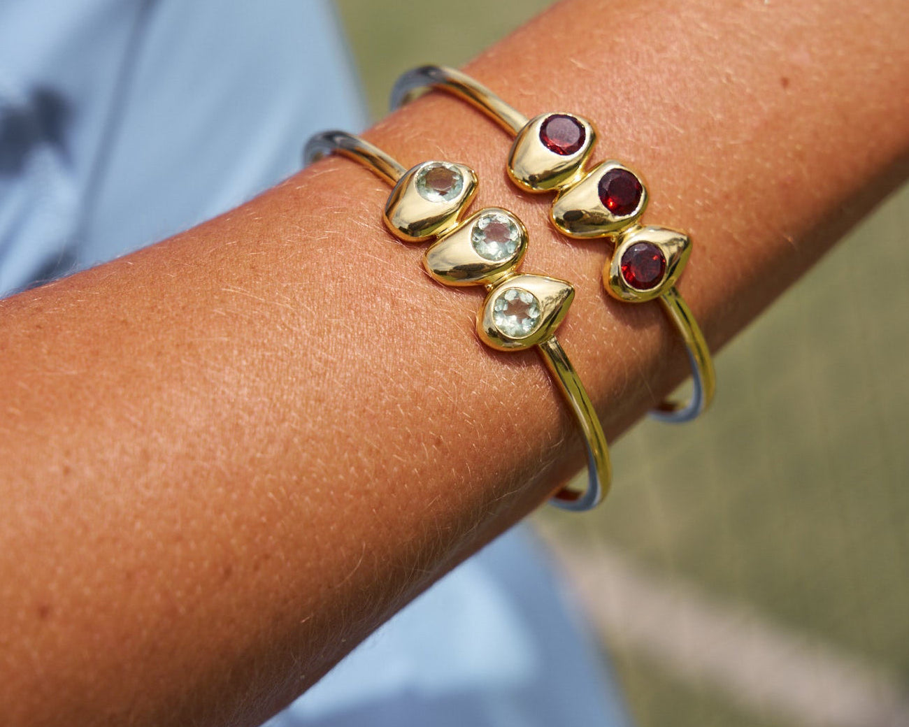 Gold bracelet with gemstones on a wrist against a blurred natural background