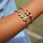 Gold bracelet with gemstones on a wrist against a blurred natural background