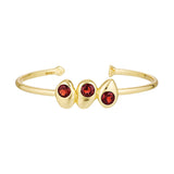 Gold bracelet with three red gemstones on a white background