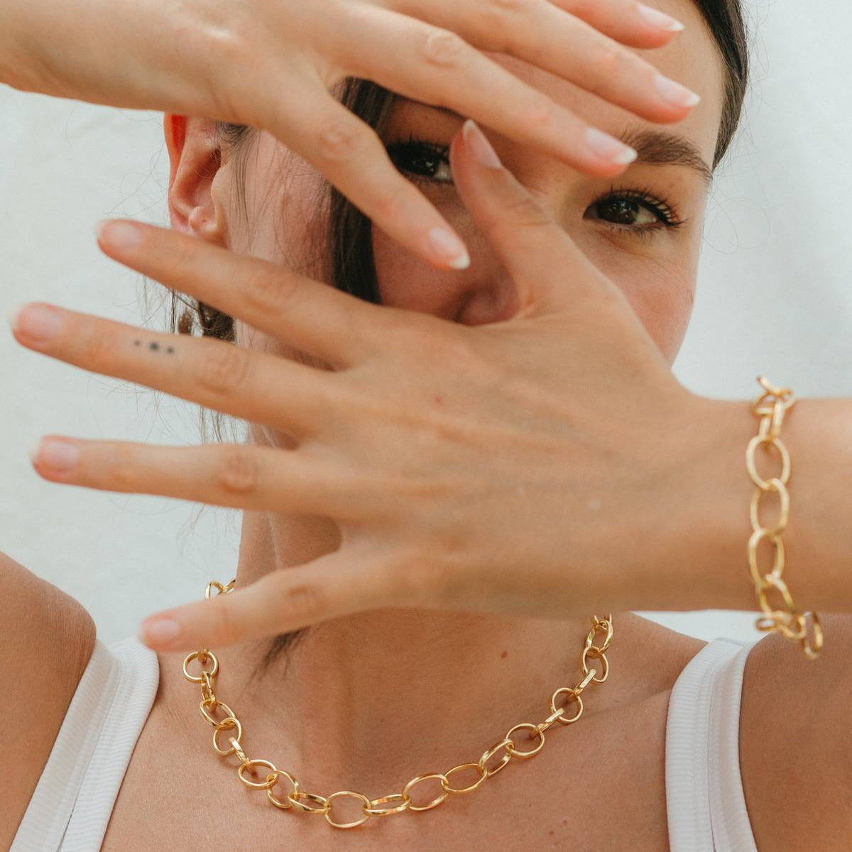 Woman wearing a gold chain necklace with a plain background