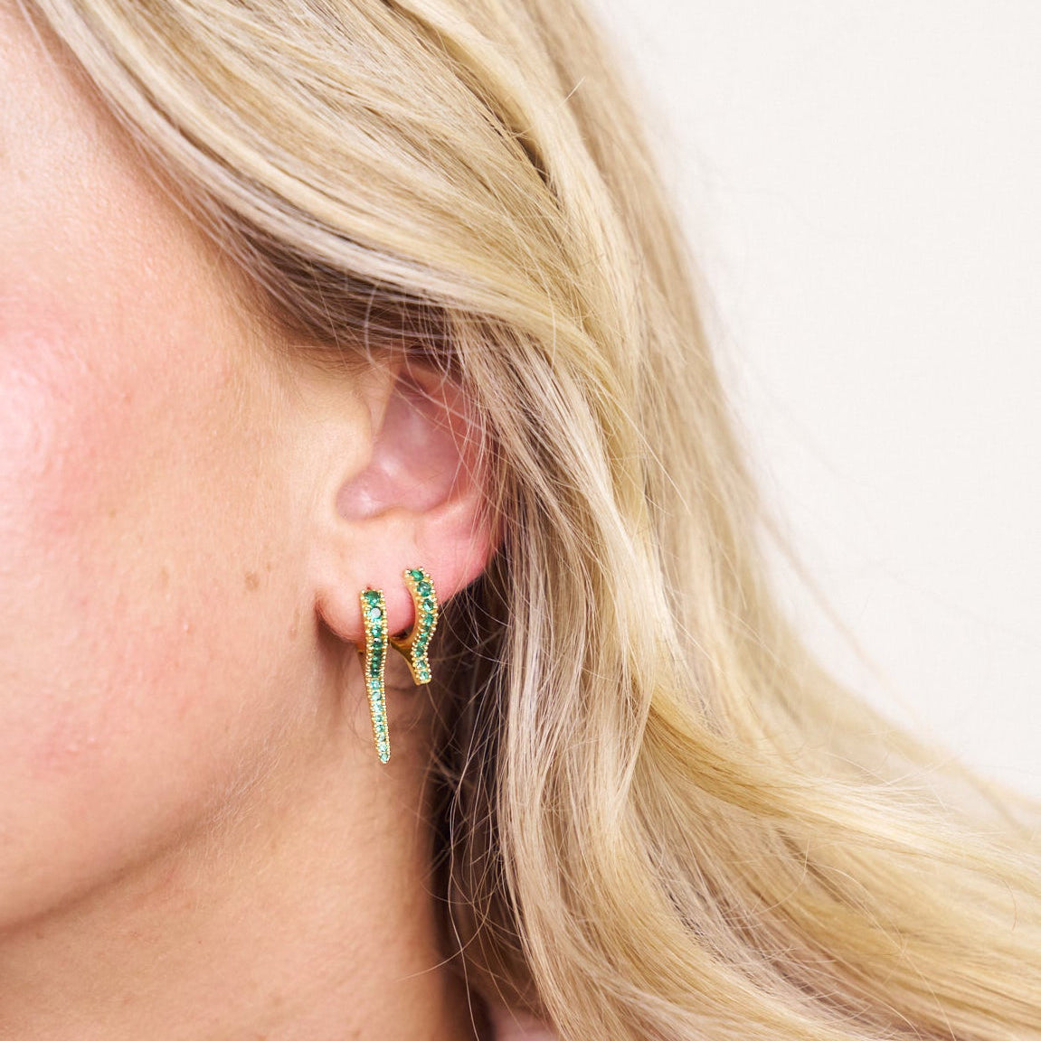 Close-up of a person wearing green gemstone hoop earring stack with a neutral background