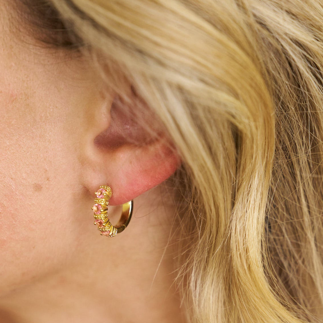 Close-up of a person wearing a gold earring with pink stones.