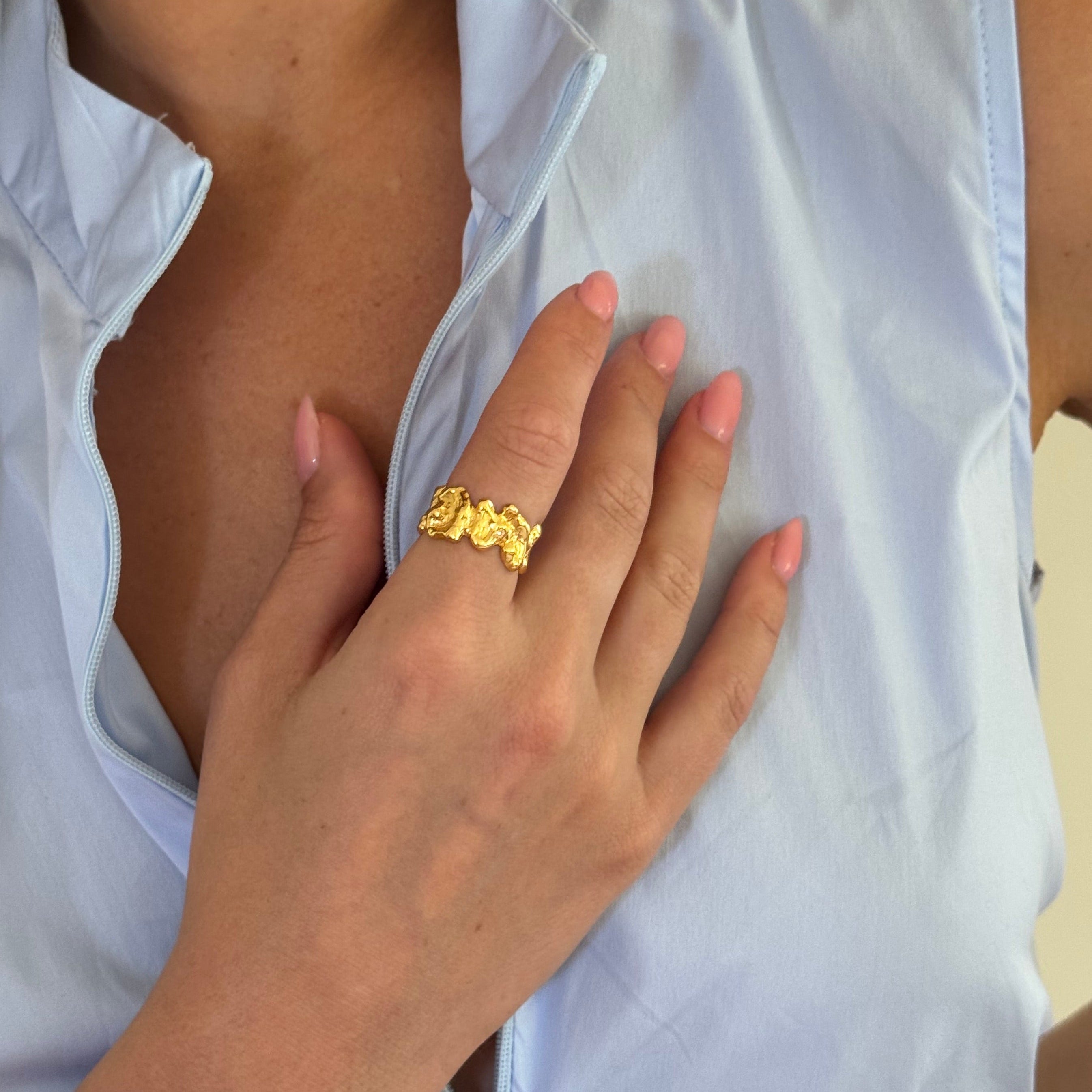 Close-up of a hand wearing a gold ring with a white garment in the background