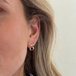 Close-up of an ear wearing a gold earring with a neutral background