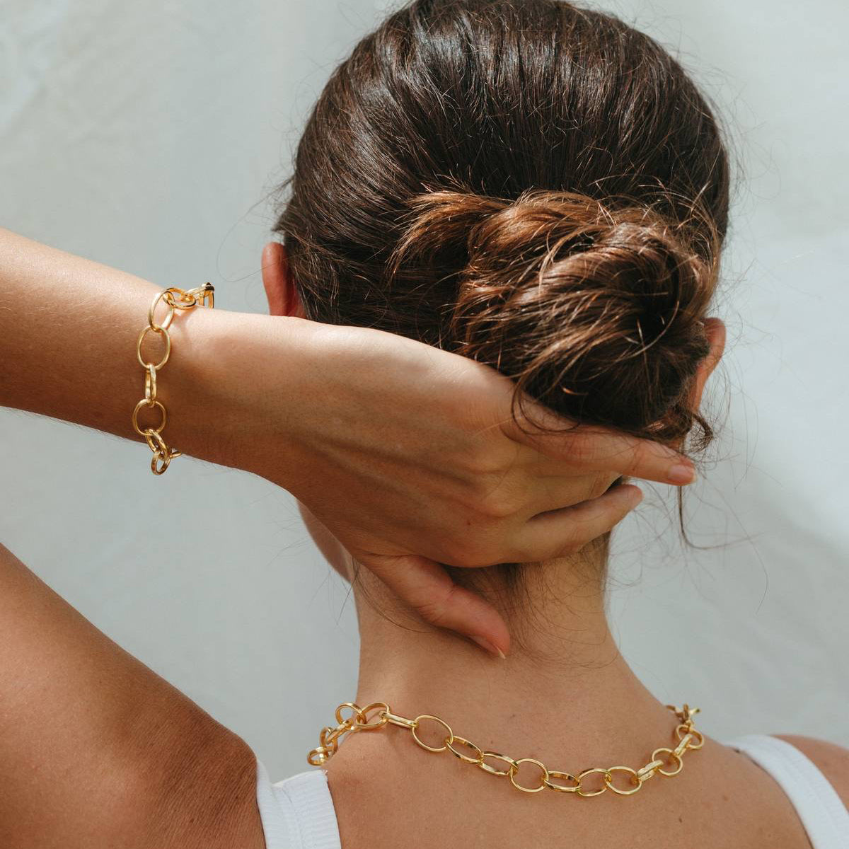 Person wearing a gold chain necklace and bracelet against a neutral background