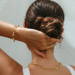 Person wearing a gold chain necklace and bracelet against a neutral background