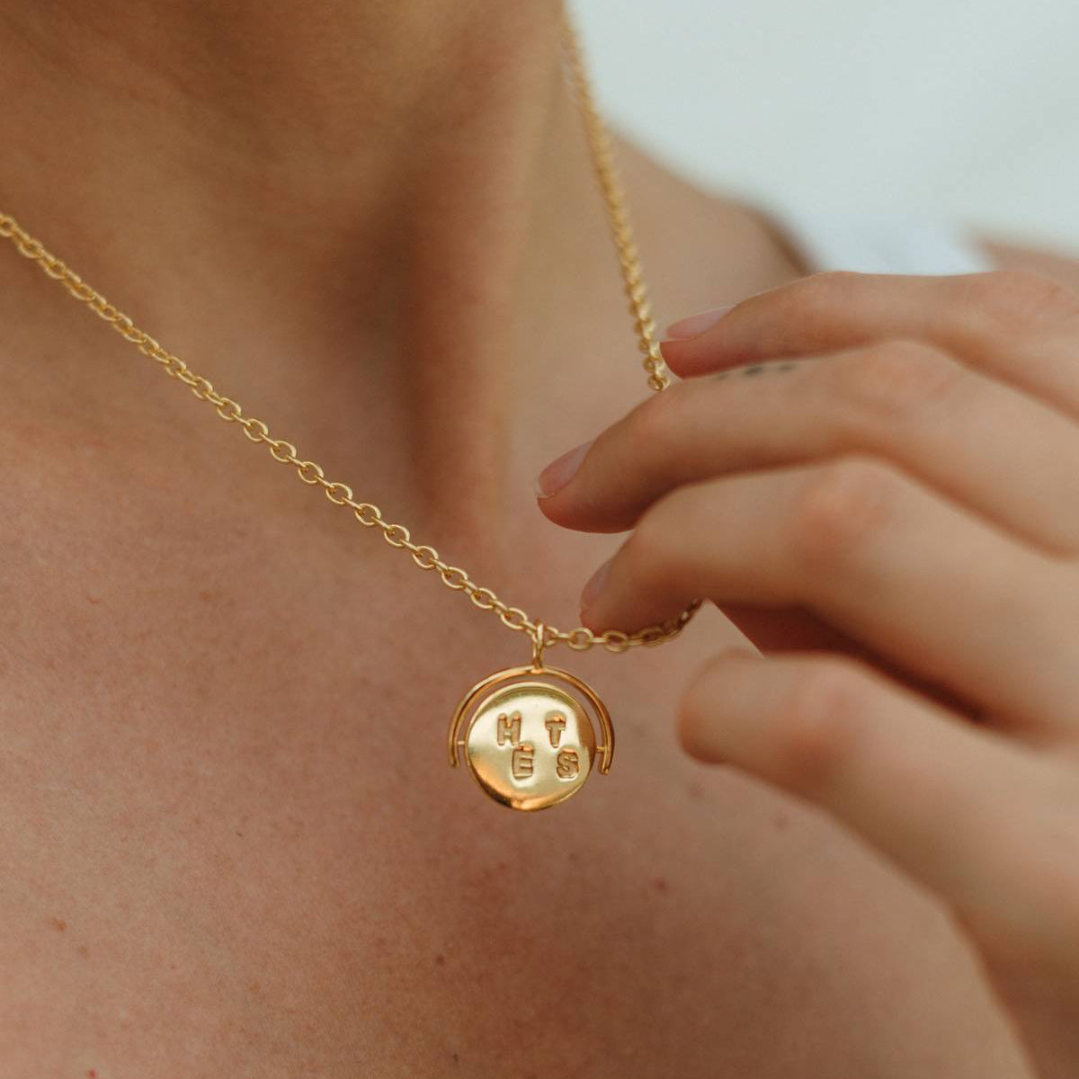 Gold necklace with a round pendant worn by a person