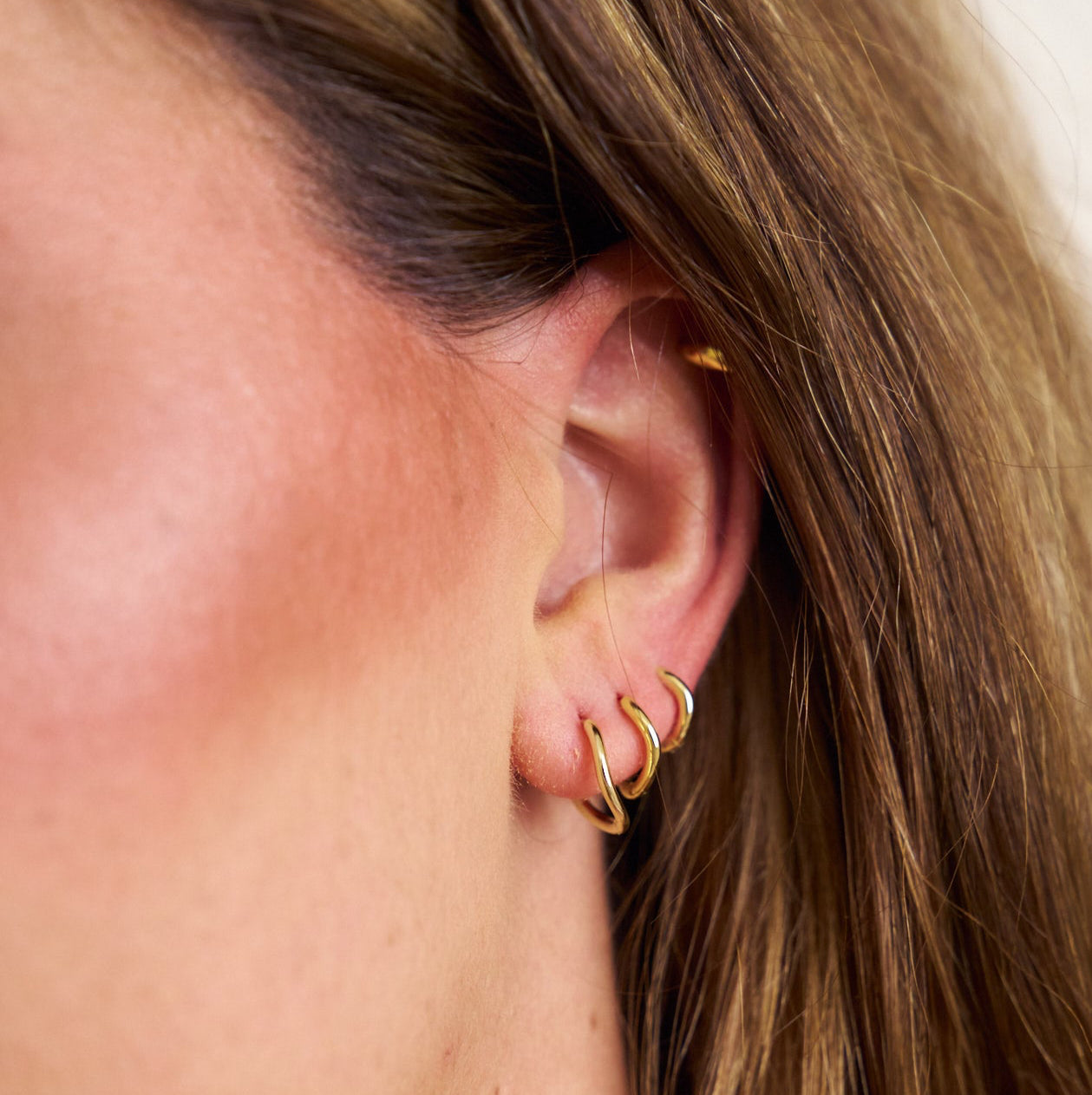 Close-up of a person wearing gold hoop earrings with a blurred background
