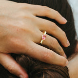 Close-up of a hand wearing a gold ring with a pink gemstone, holding hair.