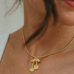 Close-up of a gold necklace with a cherry pendant on a person's neck.