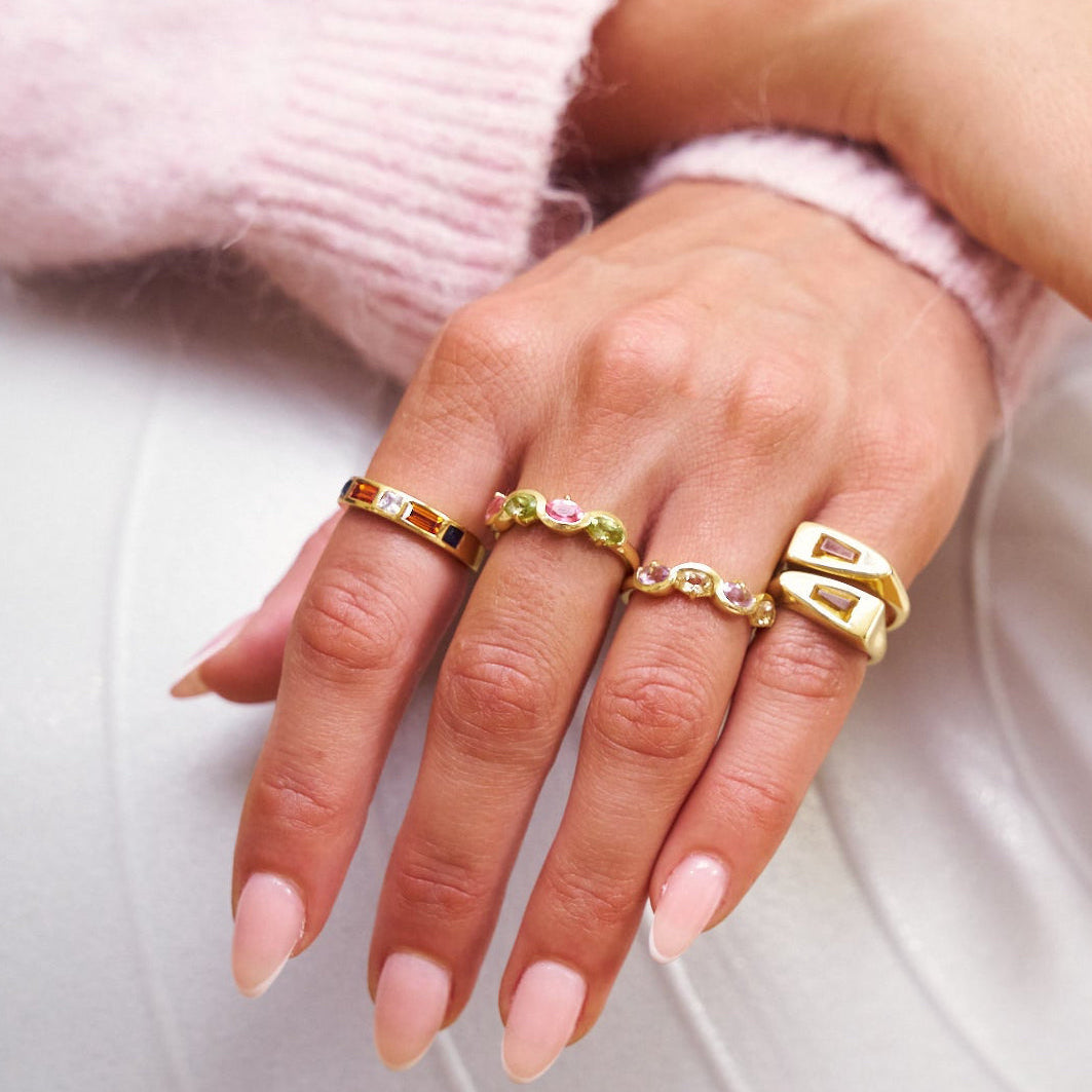 Close-up of a hand wearing multiple gold rings with gemstones on a light background