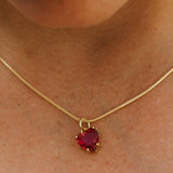 Gold necklace with a red heart-shaped pendant on a person's neck.